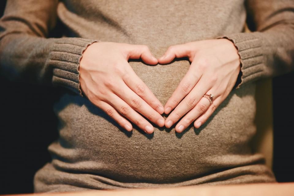 Gestante com as mãos em forma de coração sobre a barriga
